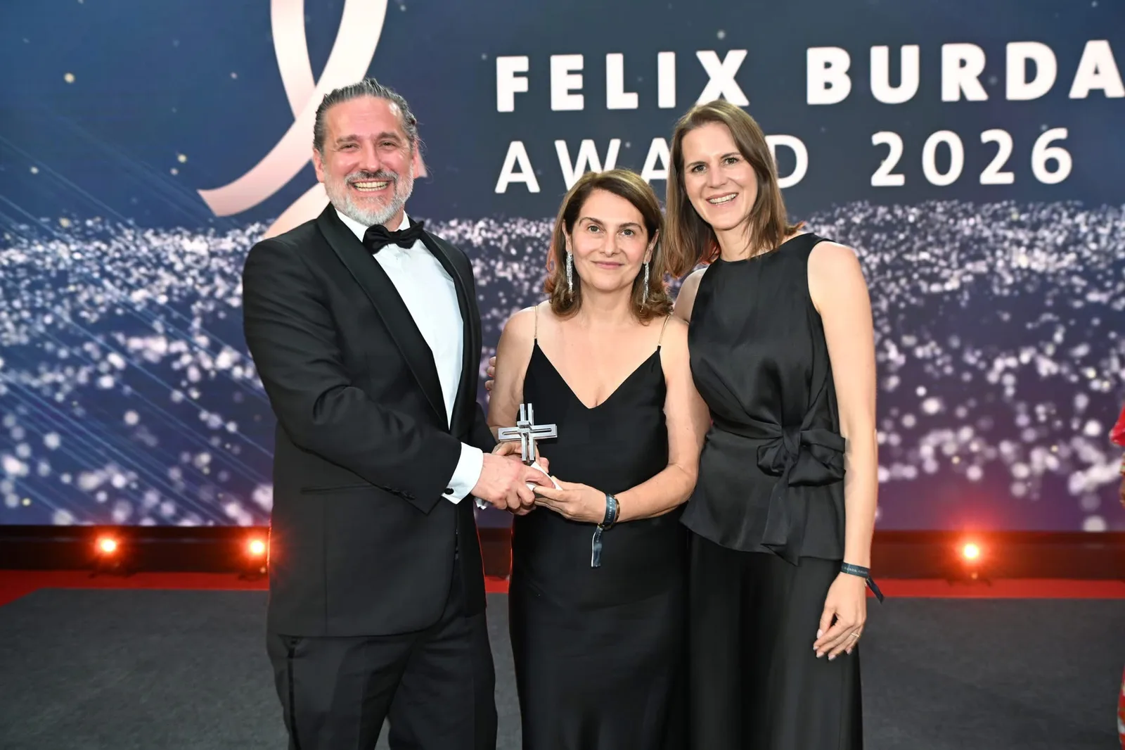 Übergabe des Felix Burda Award 2026 auf der Gala-Bühne in Berlin — Produzent Andreas Kreimaier, Dr. Katayoun Tonninger-Bahadori und Mag. Denise Daum mit der Trophäe